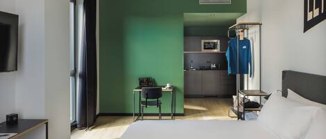 A hotel room with a bed, a desk, a chair, a TV, a kitchenette, and a wardrobe.