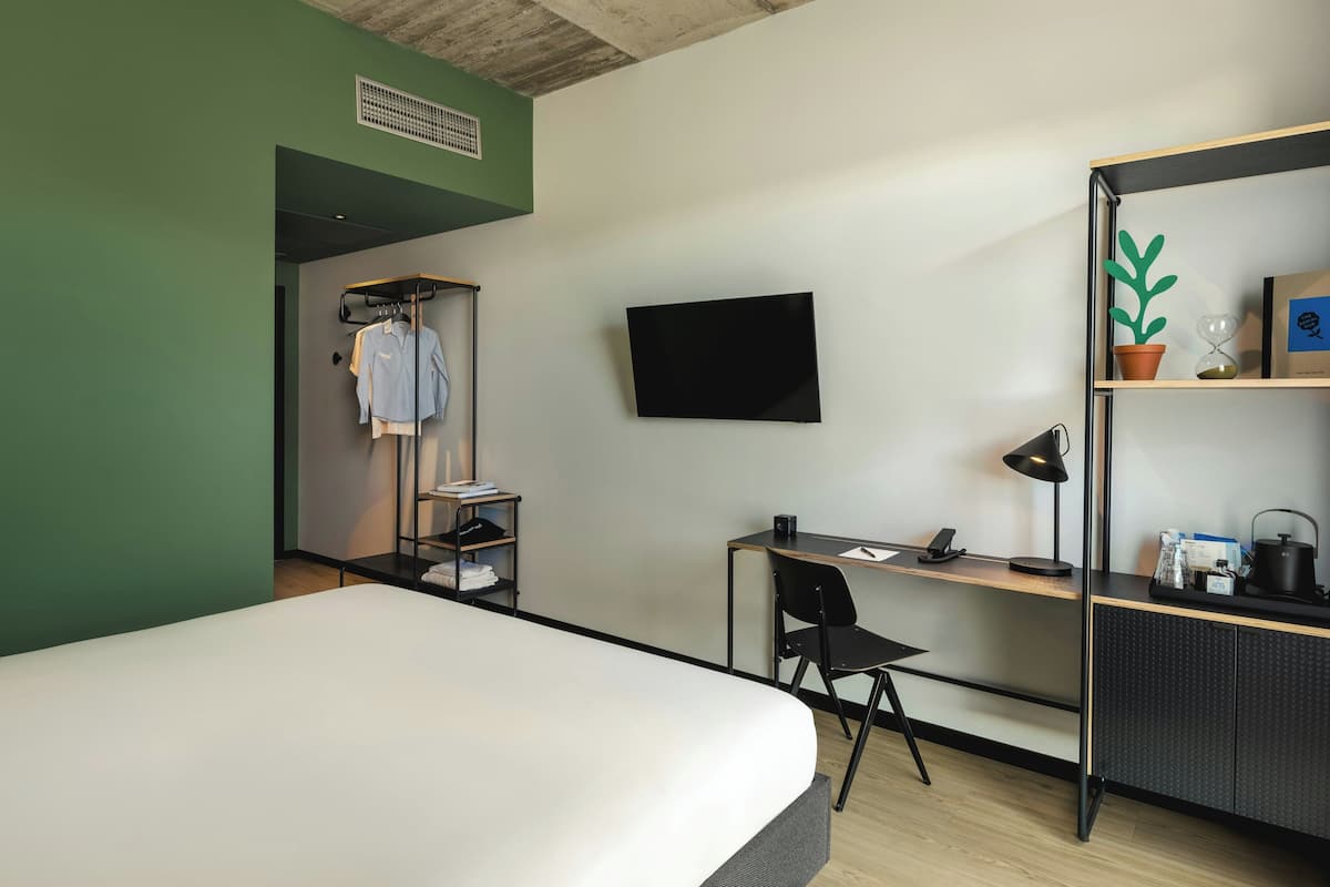 A hotel room with a bed, a desk with a chair, a TV, and a wardrobe.