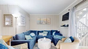 A living room with a blue sectional sofa, a round coffee table, and a beige armchair. - Tower Shores Tiny Gem (Bethany Beach)