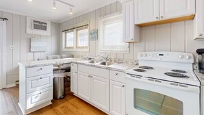 A kitchen with white cabinetry, a stove, a sink, and a window with blinds. - Tower Shores Tiny Gem (Bethany Beach)