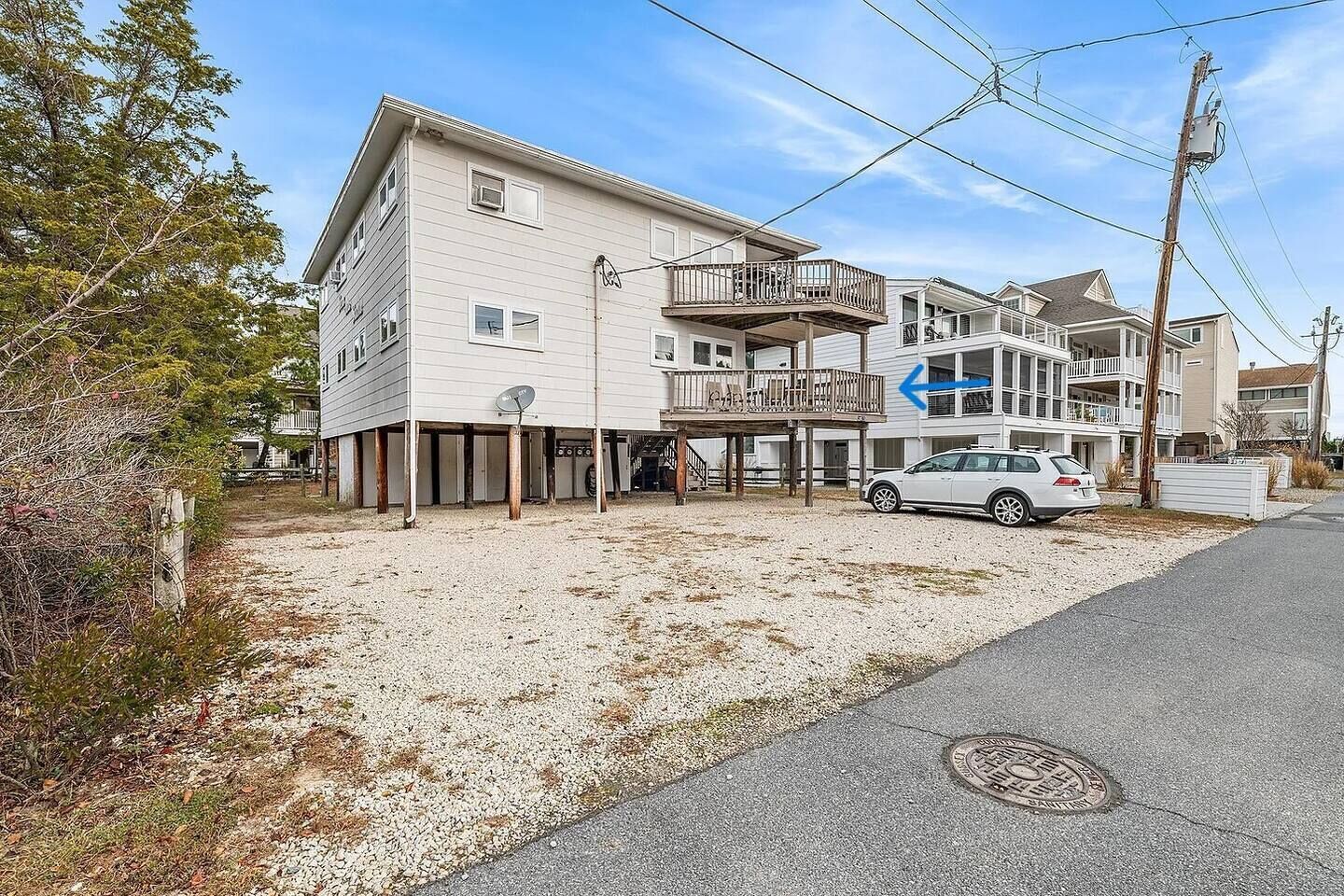 A two-story residential building with a balcony on the second floor, a gravel driveway, and a parked car.