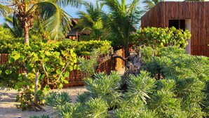 A tropical garden with palm trees, a wooden fence, and a building with a wooden exterior. - Lipsos Retreat Concierge Villa (Ixil)