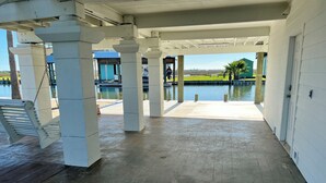 Un espace extérieur abrité, doté de piliers en béton, d’une balançoire et offrant une vue sur une étendue d’eau.