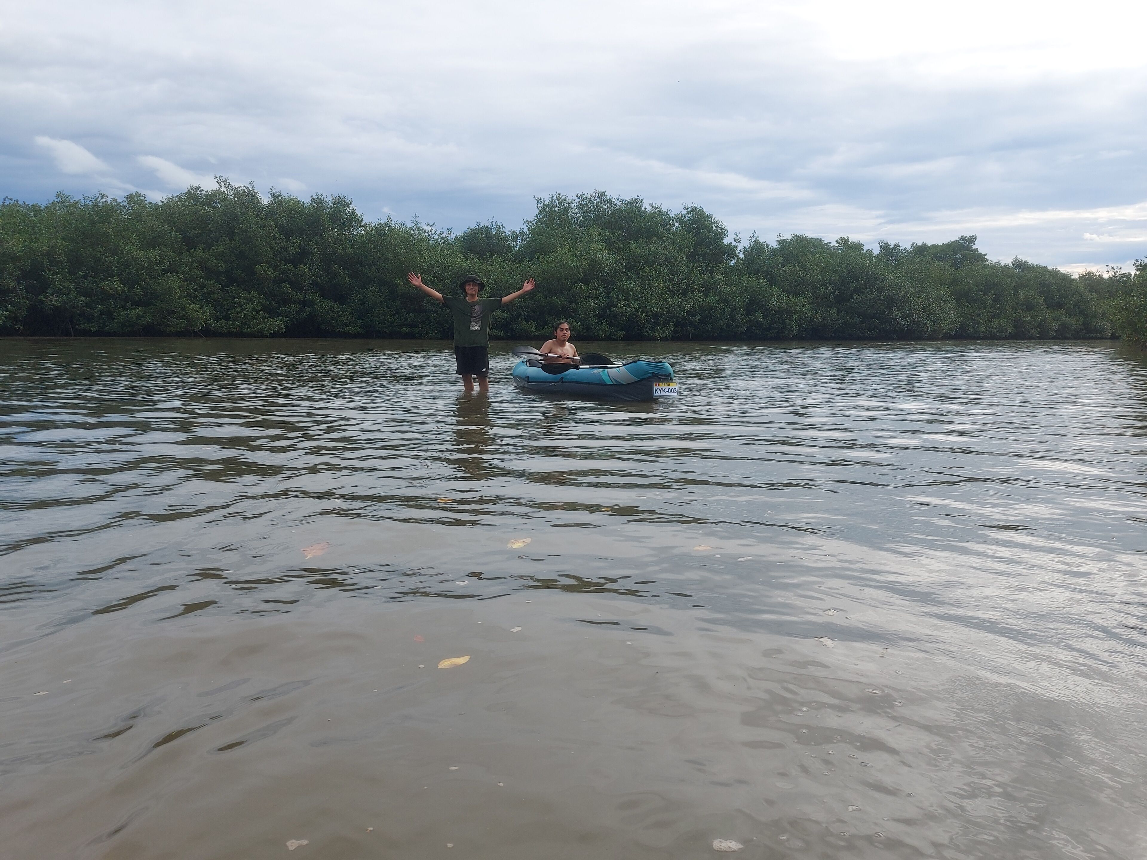 A river with a person standing in the water and a blue inflatable raft.