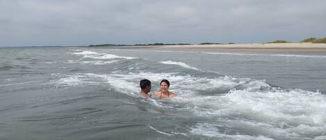 A beach with two people in the water, a sandy shore, and a cloudy sky.