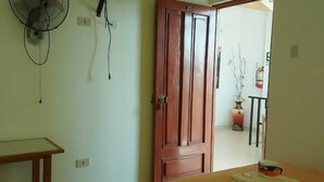 Een slaapkamer met een bed, een aan de muur bevestigde televisie, een ventilator en een deur naar een andere kamer.