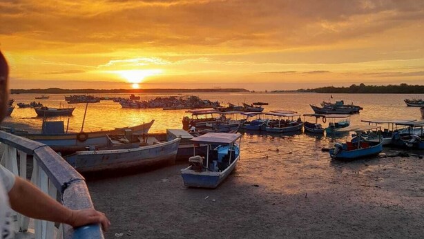 Zonsondergang vanaf een pier, met boten in het water afgemeerd.