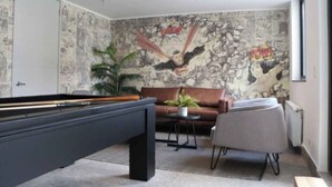 A pool table in a room with a stone-patterned wall, a brown leather sofa, and a small round table with a plant. - Painestone apartment (Puerto Natales)