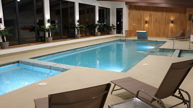 An indoor swimming pool with clear blue water, surrounded by lounge chairs and potted plants. - Painestone apartment (Puerto Natales)
