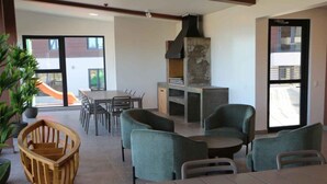 A modern dining area with a large table and chairs, a built-in grill, and a view of the outside. - Painestone apartment (Puerto Natales)