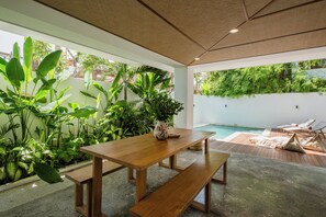 Une table en bois avec des bancs, dans un décor extérieur moderne agrémenté d’une piscine et d’une végétation luxuriante.