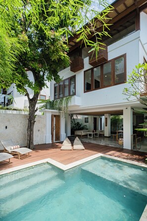 Ein modernes Haus mit Swimmingpool, Sitzgelegenheiten im Freien und einem großen Baum.