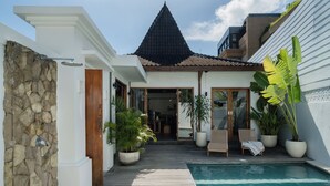 A poolside area with a wooden deck, a stone wall, and a building with a tiled roof. - Indah Sun Villa | Private Pool | 3BR | Pererenan, 2 Min to Cafés (Mengwi, Kabupaten Badung)