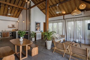 A spacious living area with a high ceiling, wooden beams, and a large window with sheer curtains.