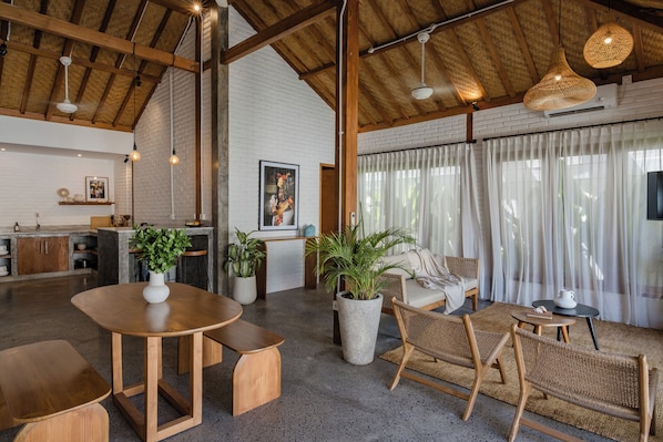 A spacious living area with a high ceiling, wooden beams, and a large window with sheer curtains.