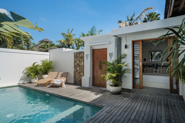 A modern poolside area with a wooden deck, lounge chairs, and potted plants.
