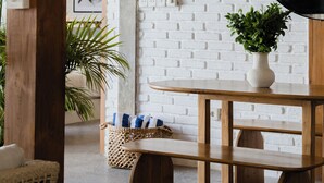 A room with a white brick wall, a round mirror, a wooden table, a bench, and a wicker basket with a plant. - Indah Sun Villa | Private Pool | 3BR | Pererenan, 2 Min to Cafés (Mengwi, Kabupaten Badung)