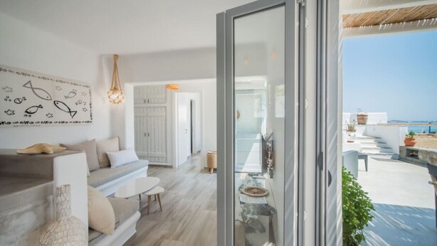 Um interior moderno com um sofá, uma mesa de jantar e vista para o mar através de uma porta de vidro.