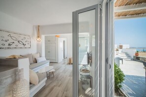 A modern interior with a sofa, a dining table, and a view of the sea through a glass door.