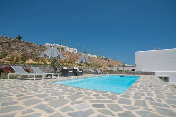 A swimming pool with stone tiles, sun loungers, and umbrellas.