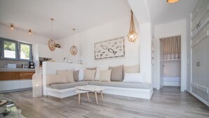 Uma sala de estar moderna com sofá seccional, mesa de centro e área de cozinha ao fundo.