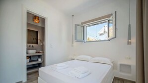 Quarto com uma cama, janela, banheiro com pia e um porta-toalhas.