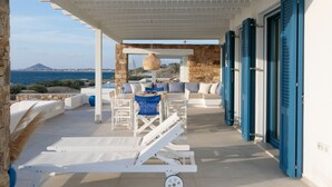 A covered outdoor seating area with white furniture and a view of the sea. - Villa Salt Mikri Vigla Naxos (Mikri Vigla)
