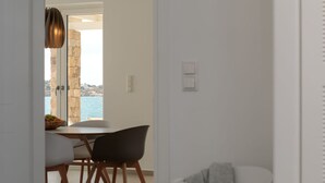 A dining area with a table and chairs, a view of the sea through a stone wall, and a door leading outside. - Villa Salt Mikri Vigla Naxos (Mikri Vigla)