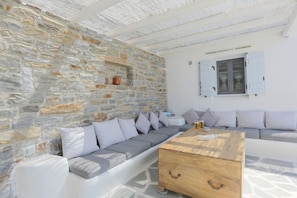 A stone-walled room with a sofa, a wooden coffee table, and a window with shutters.