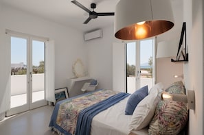Un dormitorio con cama, escritorio, silla, ventilador de techo y ventana grande.