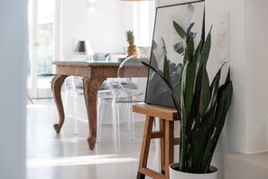 A modern interior with a wooden dining table, clear chairs, a potted plant, and a framed artwork on a stand.