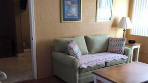 Een woonkamer met een groene bank, een houten salontafel en twee foto's in lijsten aan de muur.