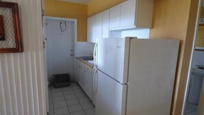 Une cuisine de taille réduite avec des meubles blancs, un réfrigérateur et un sol carrelé.