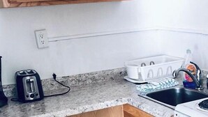 A kitchen with a granite countertop, a toaster, a dish rack, and a sink. - Queen Studio-Full Kitchen,Tiki Area, Overlooking the Beach (Pompano Beach)