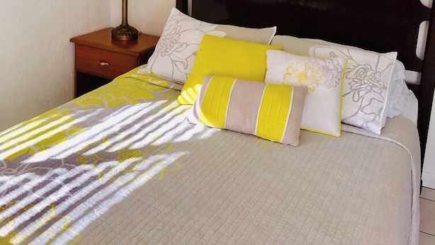 A bed with a patterned bedspread, two pillows with floral designs, and a bedside table with a lamp. - Queen Studio-Full Kitchen,Tiki Area, Overlooking the Beach (Pompano Beach)