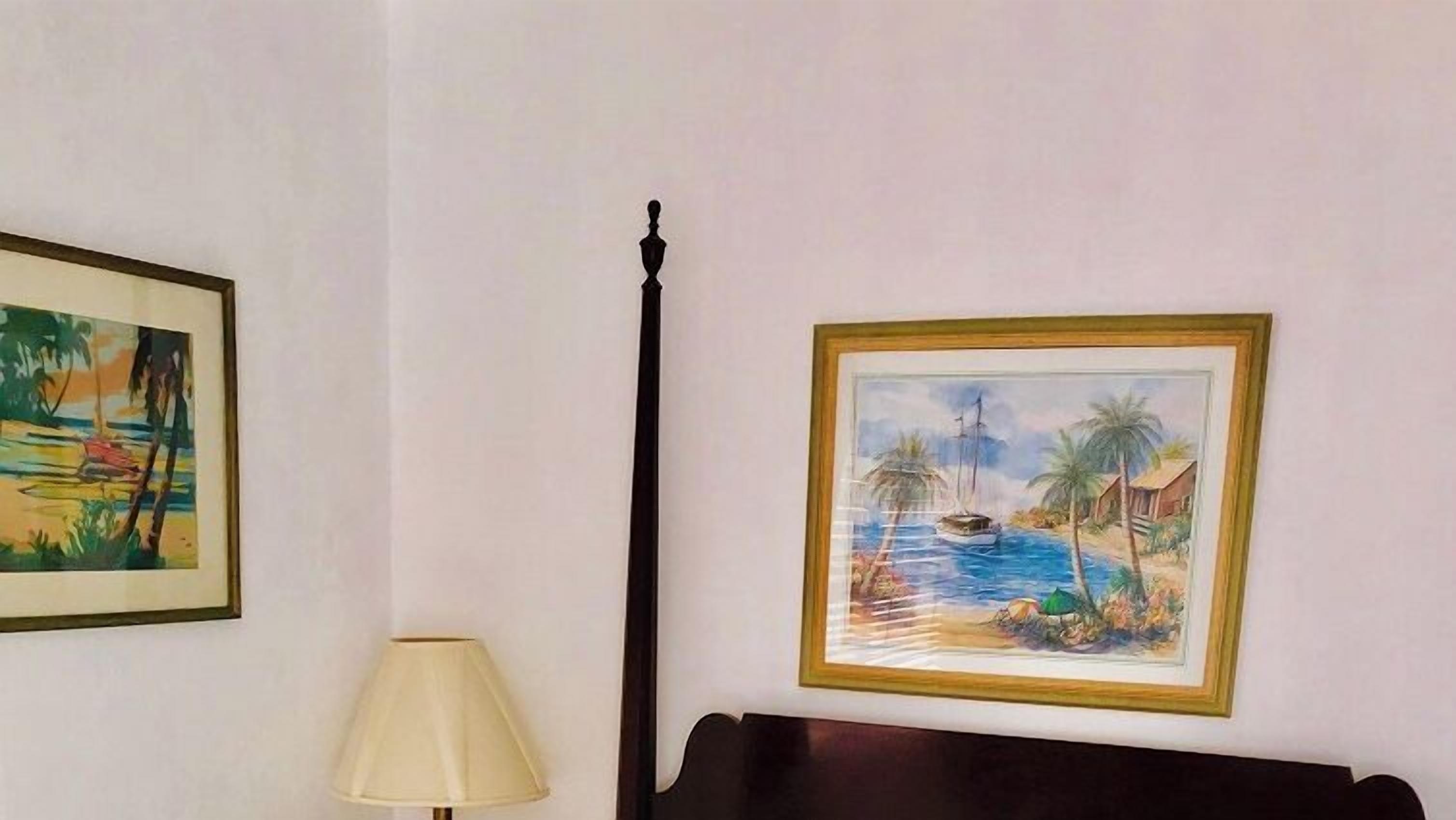 A room with a bed, a lamp, and two framed pictures on the wall.