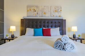 Een hotelkamer met een groot bed, een donker hoofdeinde en drie bloemschilderijen aan de muur.