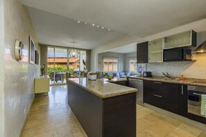 Een moderne keuken met donkere kastjes, een granieten werkblad en een centraal eiland. Een eethoek met een tafel en stoelen is zichtbaar door de glazen deuren.