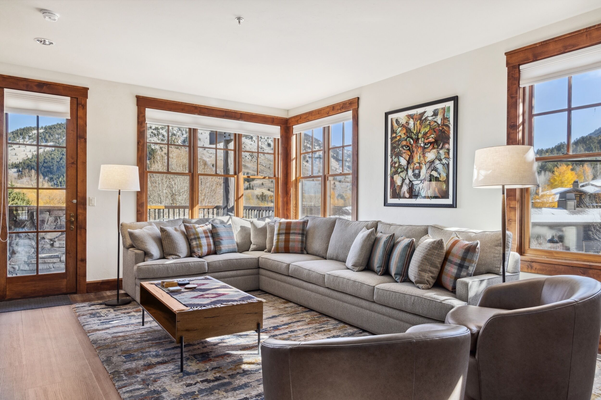 A spacious living room with a large sectional sofa, a coffee table, and a view of a mountainous landscape through large windows.
