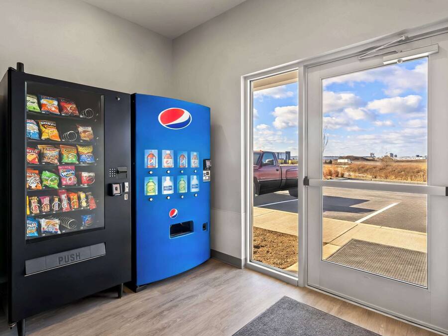 Una macchina distributrice con snack e bevande, una macchina Pepsi blu e vista su un parcheggio attraverso una porta di vetro.