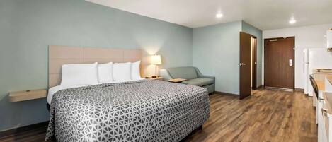 Una habitación de hotel con cama, mesita de noche, sofá, escritorio y kitchenette.