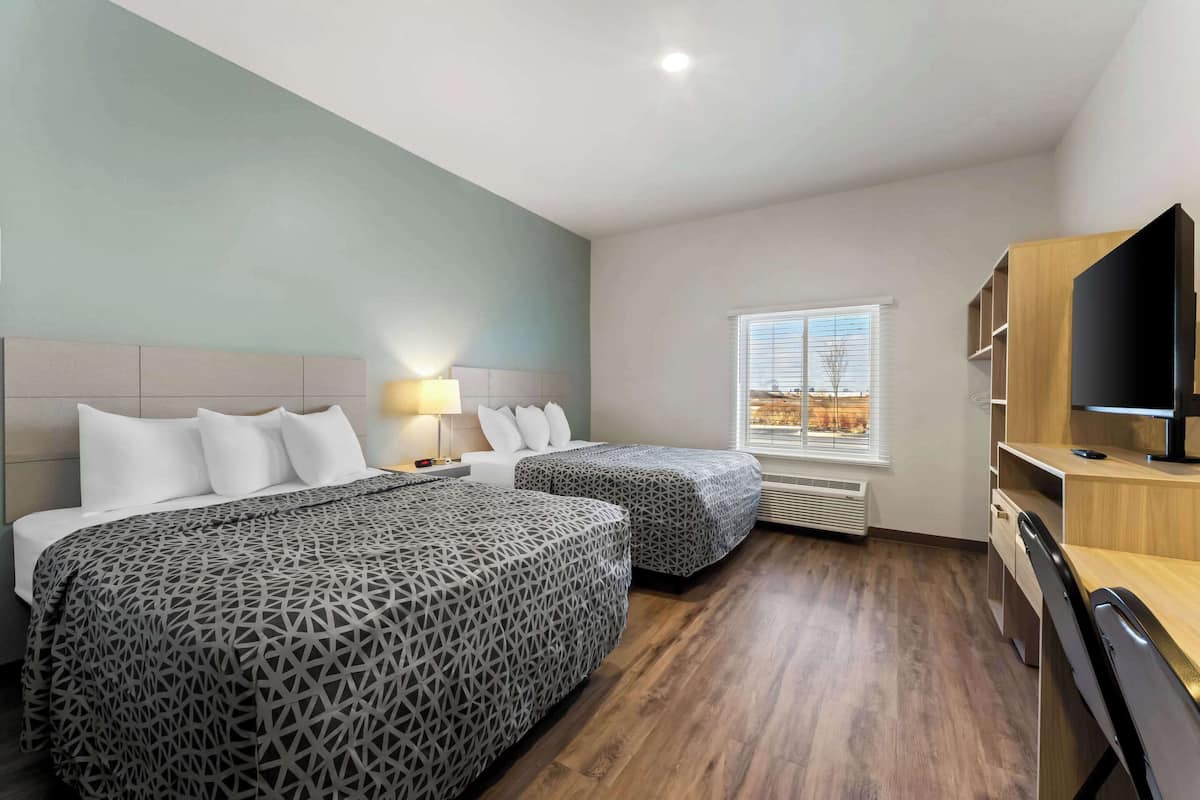 Une chambre d’hôtel avec deux lits, un bureau, une télévision et une fenêtre avec des stores.