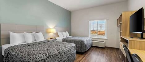 A hotel room with two beds, a desk, a TV, and a window with blinds.