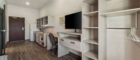 A modern, well-lit room with a wooden floor, a desk with a chair, a television, and built-in shelving units.