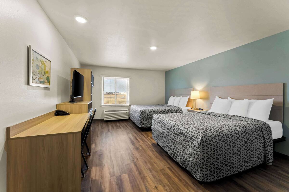 Une chambre d’hôtel avec deux lits, un bureau, une télévision et une fenêtre avec des stores.