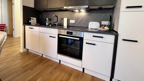 Moderni keittiö, jossa on valkoiset kaapit, musta työtaso ja sisäänrakennettu uuni.