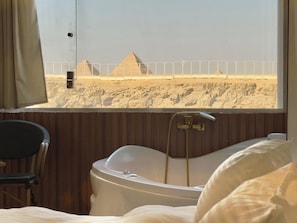 A hotel room with a bathtub, a chair, and a view of pyramids. - Shiny Pyramids Boutique Hotel (Giza)