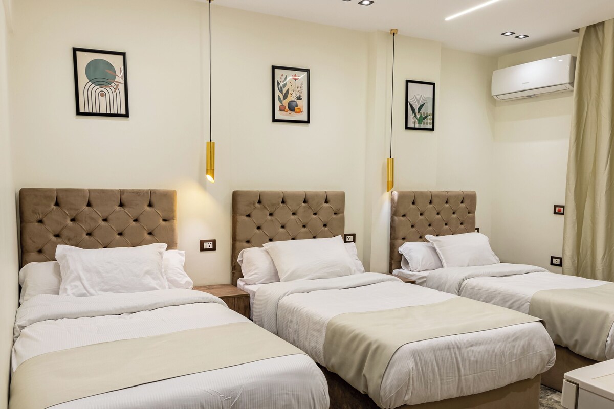 Ein Hotelzimmer mit drei Betten, einer Wand-Klimaanlage und zwei Pendelleuchten.