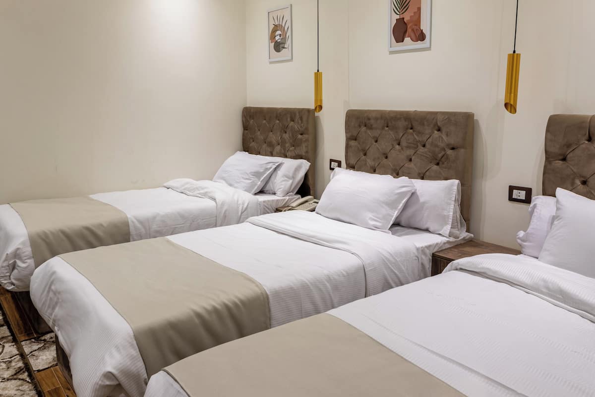 A hotel room with two beds, a small bedside table, a wall-mounted light, and two framed artworks.