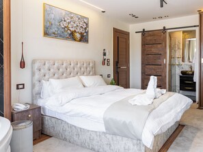 A bedroom with a large bed, a bedside table with a phone, a wall-mounted painting, and a wooden door. - Shiny Pyramids Boutique Hotel (Giza)